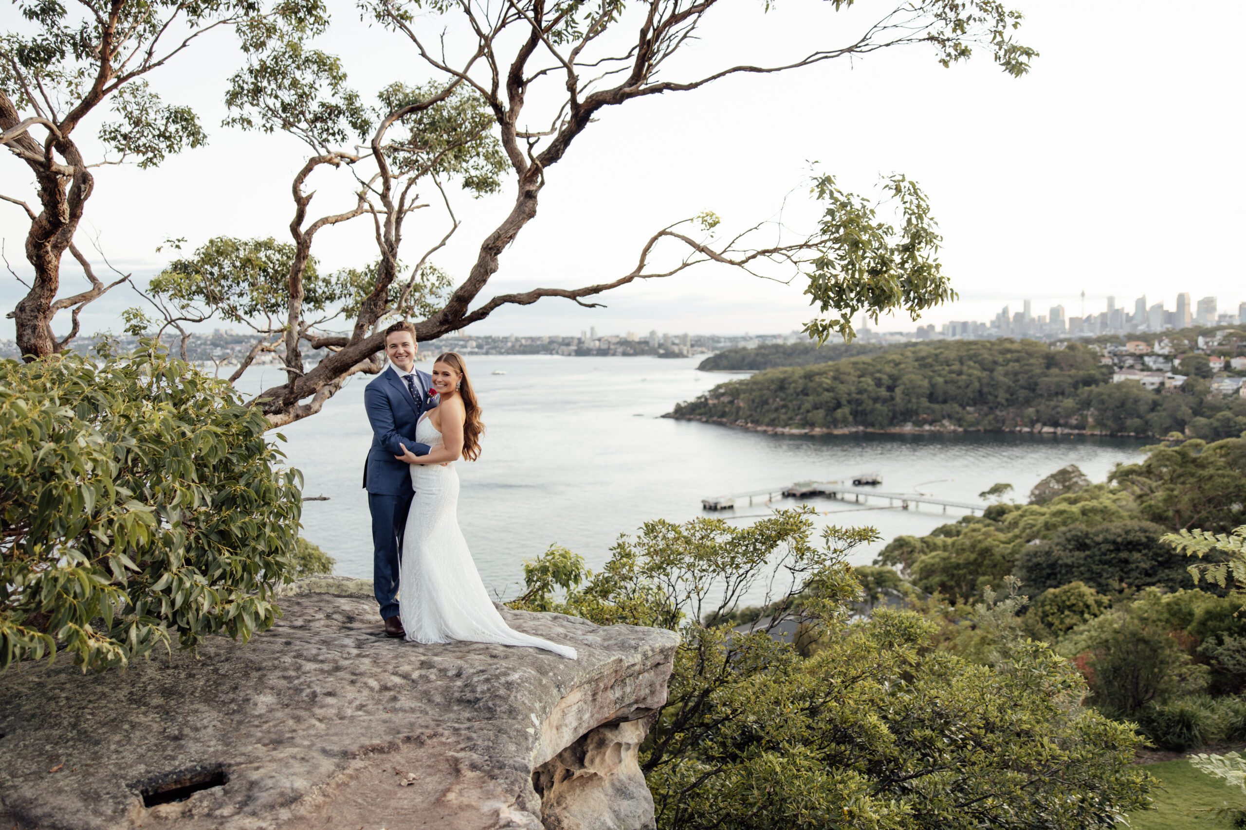 Bride and groom standing on a rock with Sydney harbour in the background